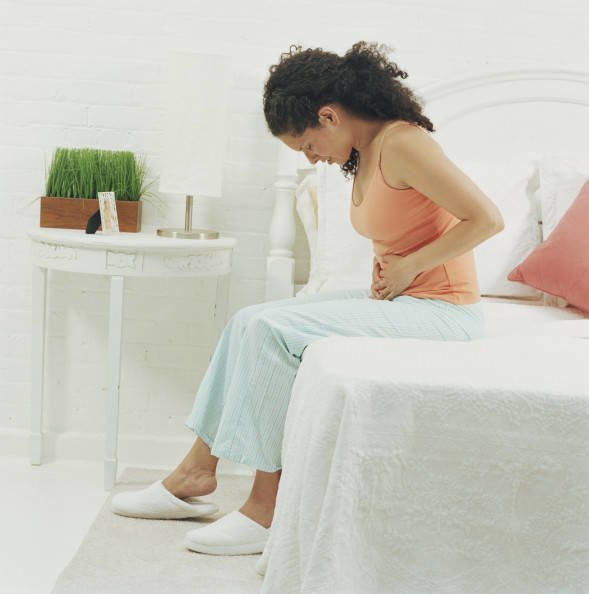 Woman sitting on bed holding stomach, head bowed