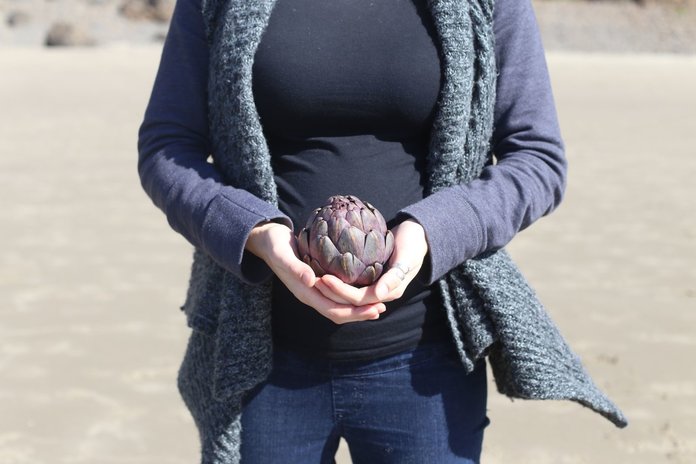 Беременная девушка с плодом артишока в руках